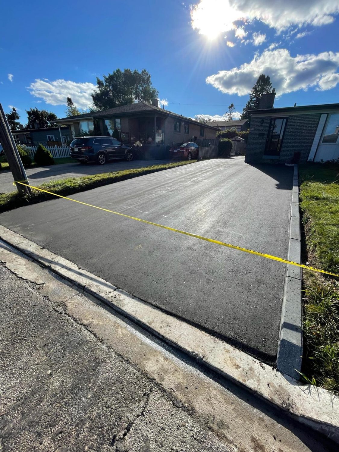 Freshly paved residential driveway with concrete curb edging, taped off to cure